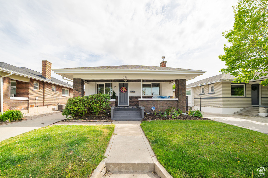 Bungalow-style house featuring brick siding, a front lawn, a porch, and cooling unit