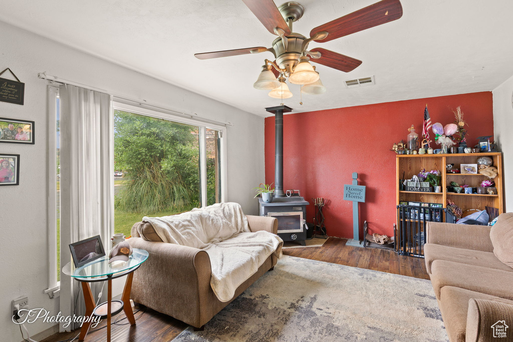 Living area with wood finished floors, a wood stove, and a ceiling fan