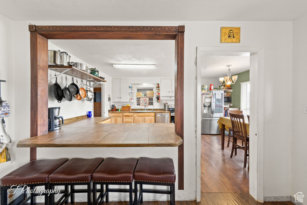 Kitchen featuring stainless steel appliances, a kitchen breakfast bar, wood finished floors, a sink, and tile countertops