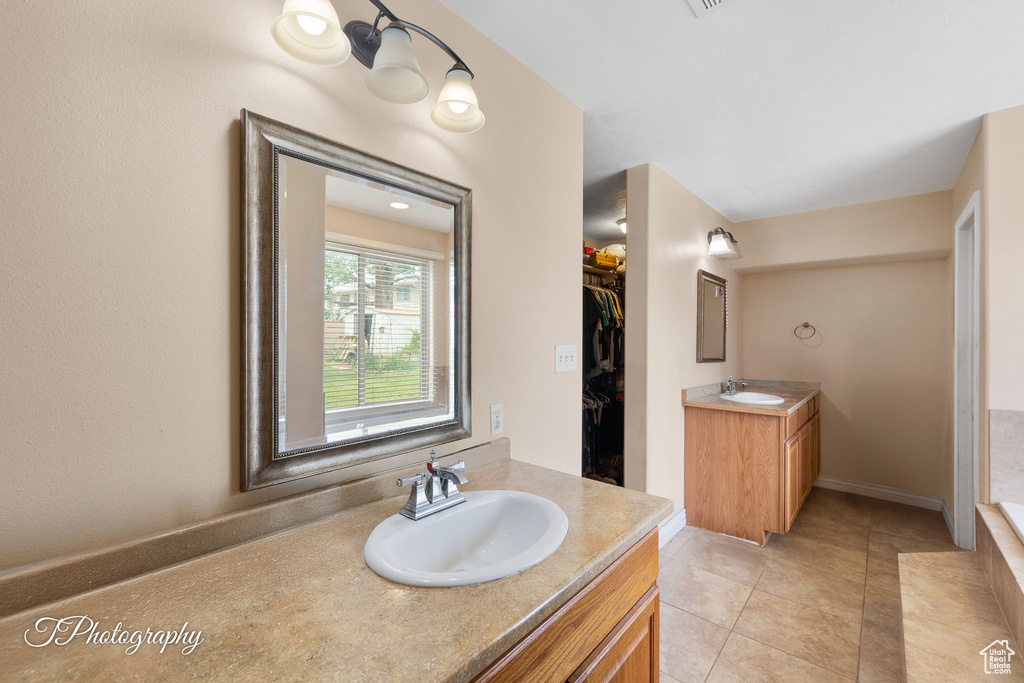 Bathroom featuring two vanities, tile patterned floors, a walk in closet, and baseboards