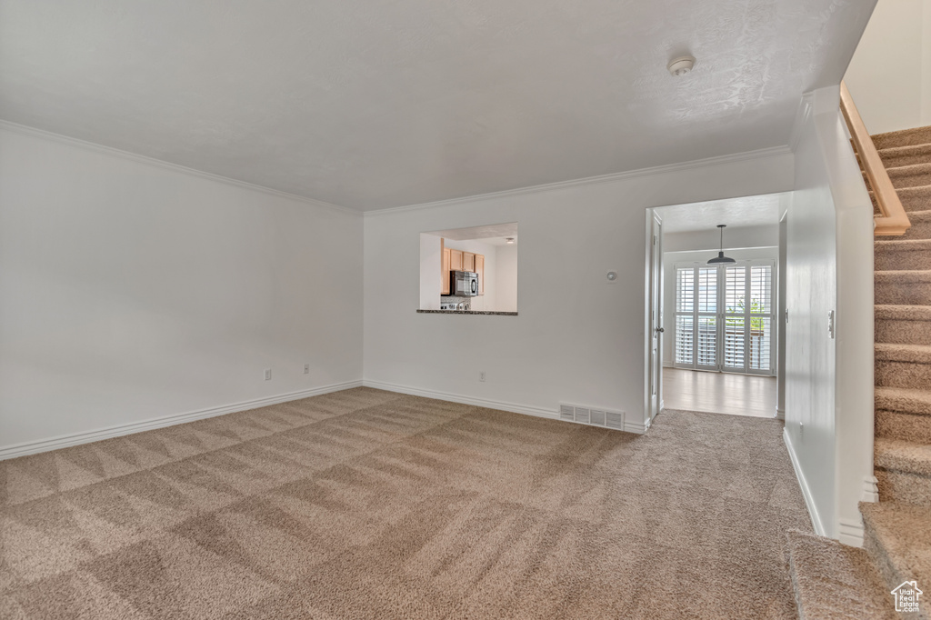 Empty room with stairs, carpet, crown molding, and baseboards