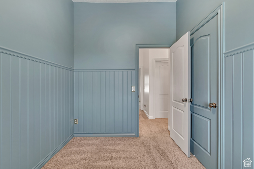 Empty room featuring light carpet and a wainscoted wall