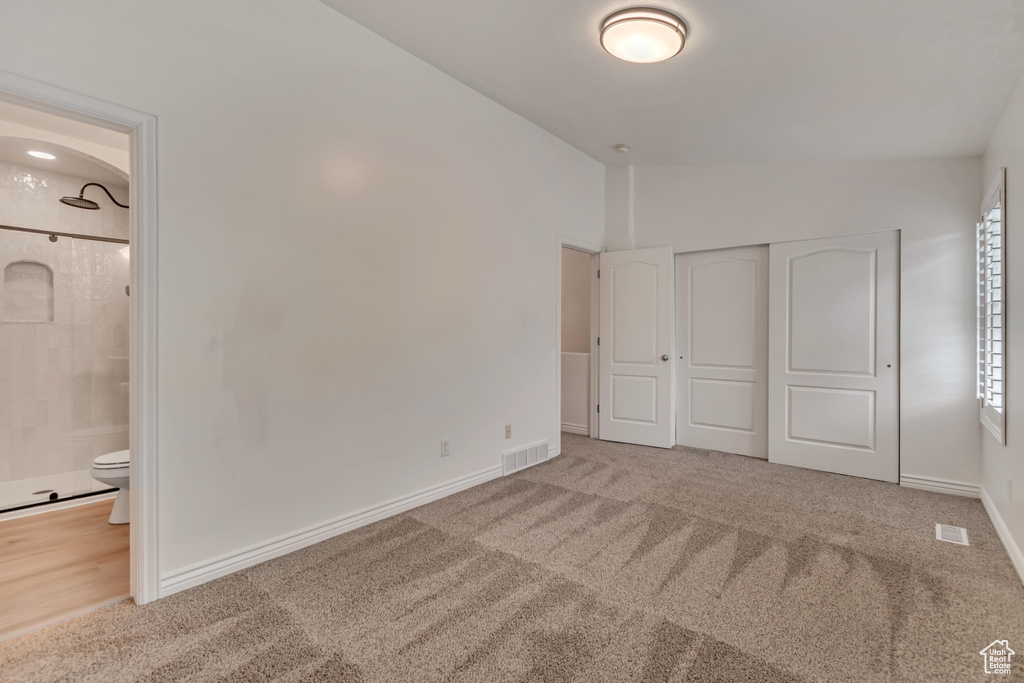 Unfurnished bedroom featuring vaulted ceiling, carpet flooring, a closet, and connected bathroom