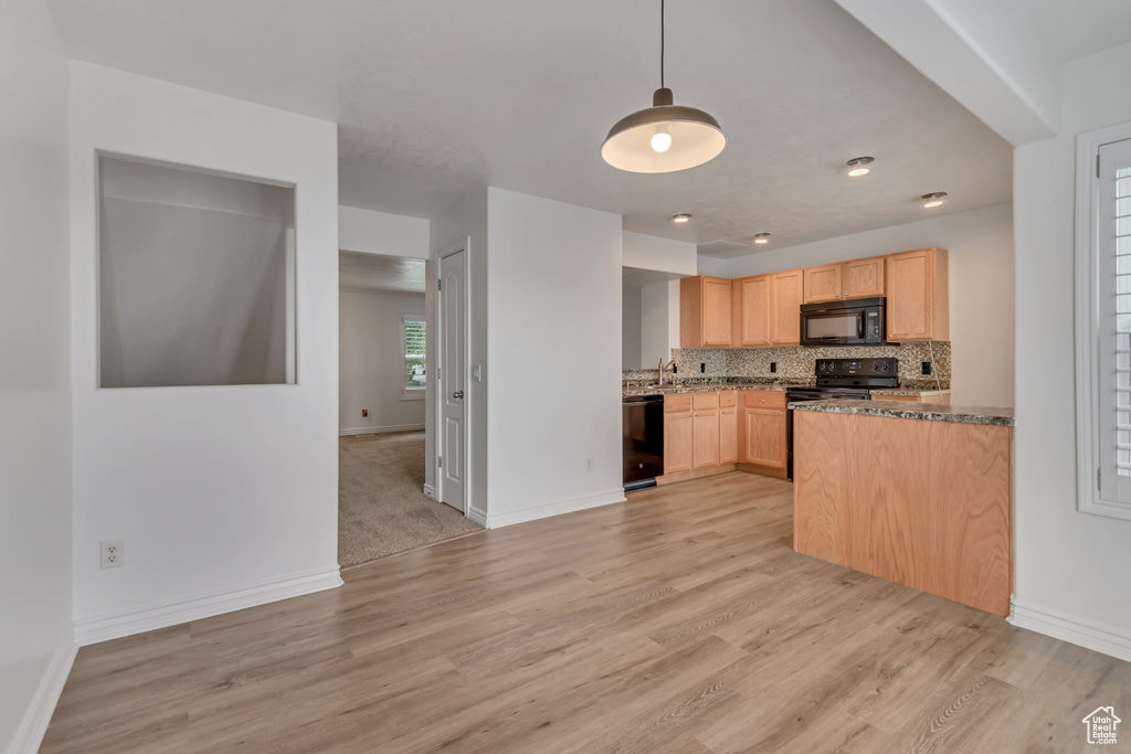 Kitchen featuring black appliances, light brown cabinets, light wood-type flooring, and decorative backsplash