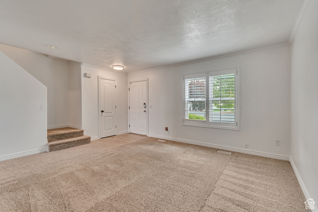 Unfurnished living room with light carpet, stairway, baseboards, and ornamental molding