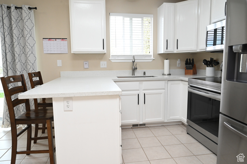 Kitchen featuring a peninsula, light tile patterned floors, a breakfast bar, a sink, and stainless steel appliances