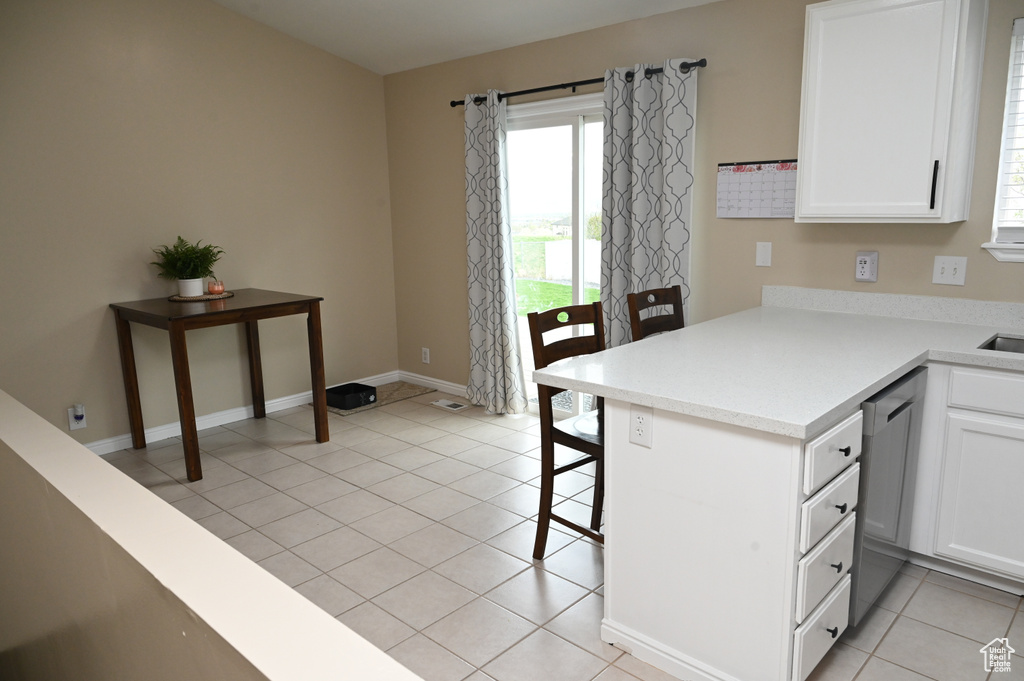 Kitchen featuring white cabinets, light countertops, stainless steel dishwasher, and a kitchen bar