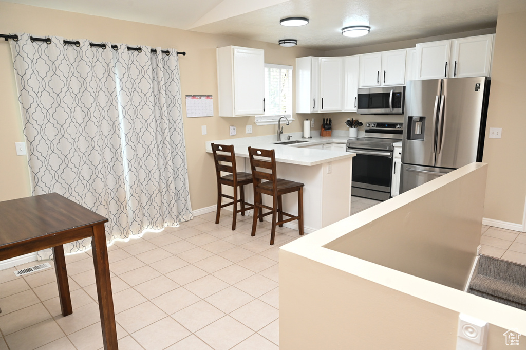 Kitchen featuring a peninsula, stainless steel appliances, a kitchen breakfast bar, white cabinetry, and light tile patterned flooring