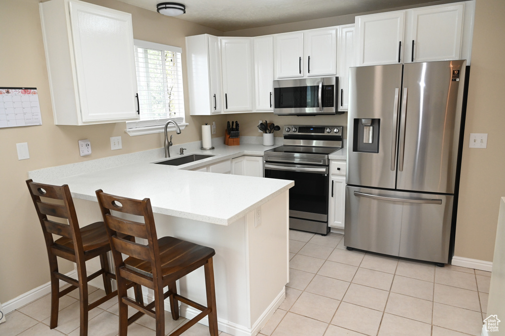 Kitchen with stainless steel appliances, a sink, a peninsula, light countertops, and white cabinets