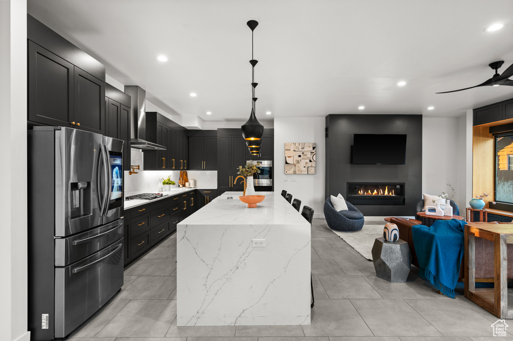 Kitchen with recessed lighting, light stone counters, stainless steel appliances, wall chimney range hood, and dark cabinetry