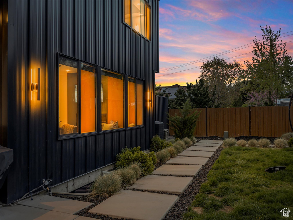 View of side of home with cooling unit, a lawn, board and batten siding, and fence