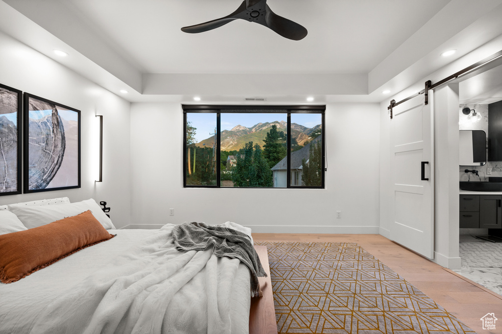 Bedroom with a barn door, light wood-type flooring, baseboards, and recessed lighting