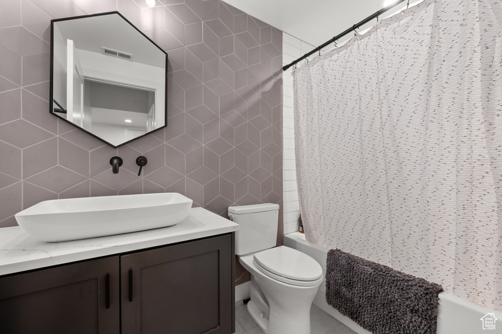 Full bathroom featuring shower / bath combo, visible vents, toilet, tile walls, and vanity