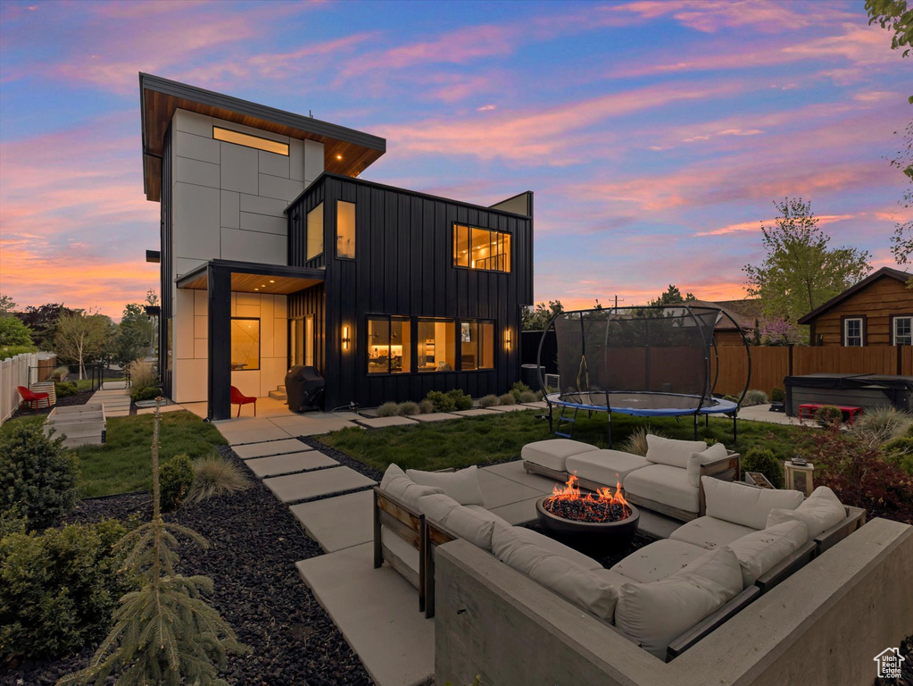 Rear view of property with a trampoline, board and batten siding, a hot tub, a patio, and an outdoor living space with a fire pit