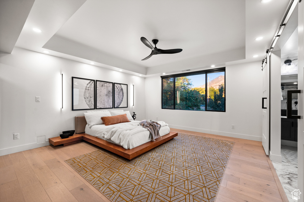 Bedroom with a barn door, recessed lighting, a tray ceiling, and baseboards