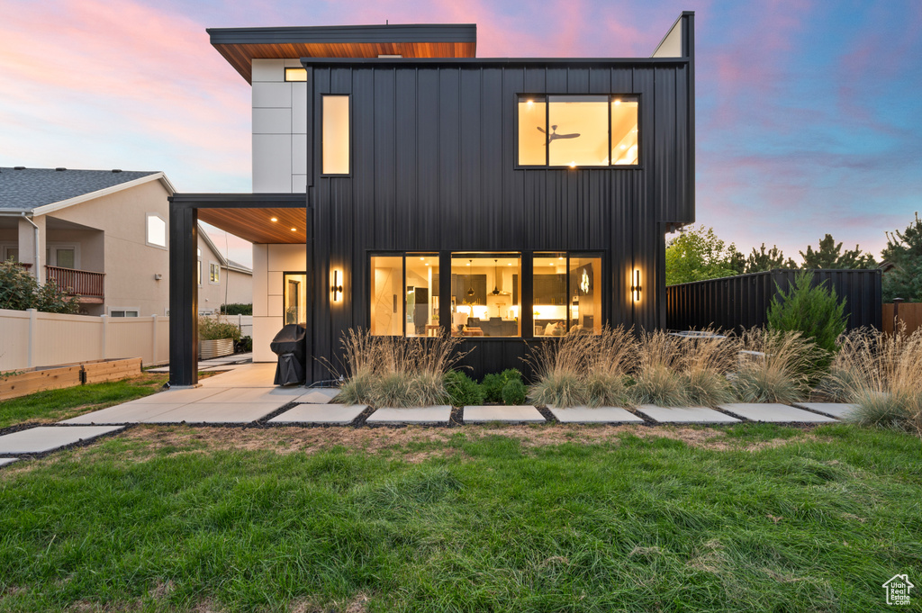 Back of house with a lawn, a patio, board and batten siding, and fence