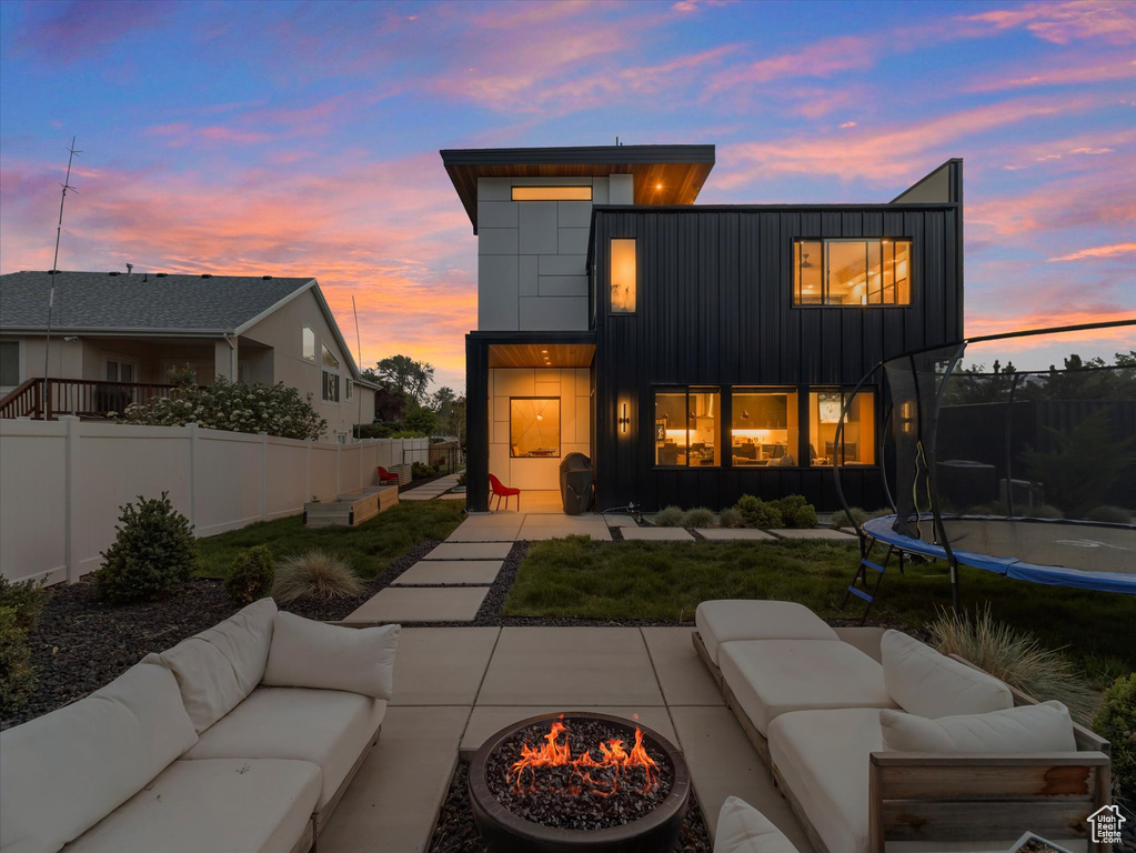 Back of house at dusk with an outdoor living space with a fire pit, a trampoline, board and batten siding, and fence