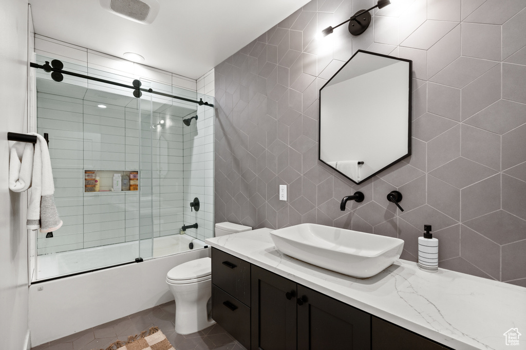 Full bath with shower / bath combination with glass door, vanity, tile patterned floors, toilet, and backsplash
