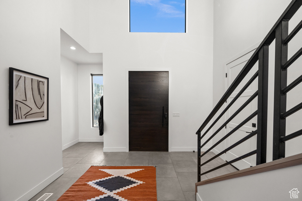 Foyer with a towering ceiling, baseboards, tile patterned flooring, and stairs