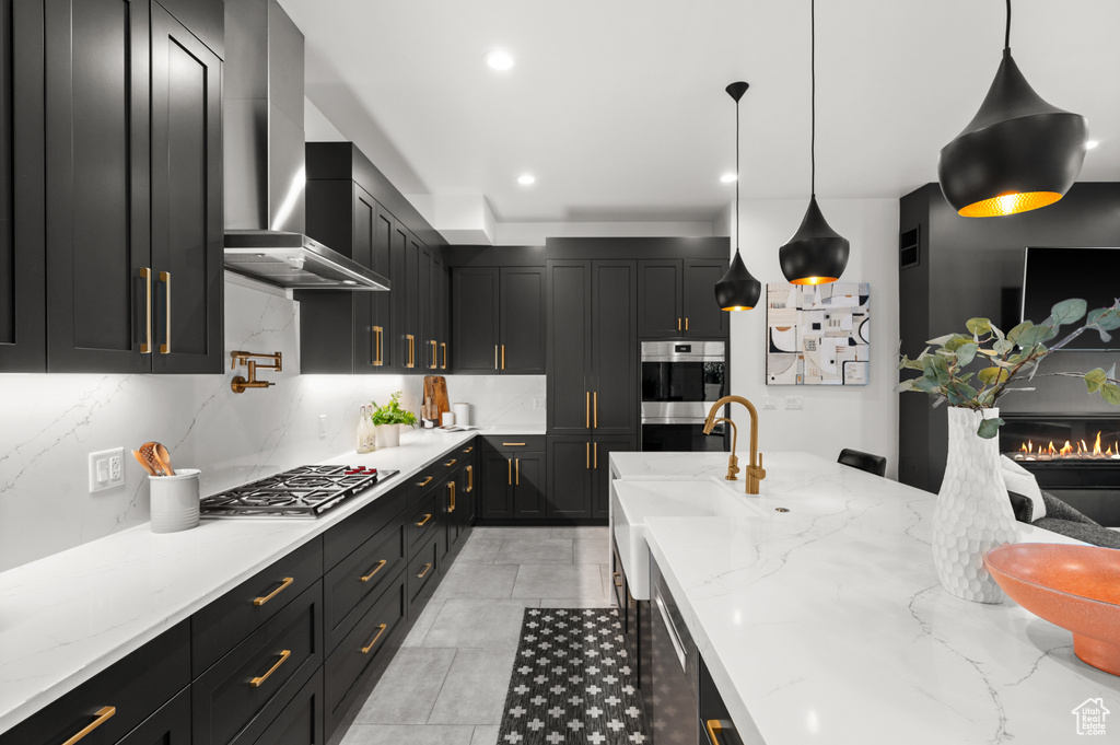 Kitchen with a sink, dark cabinetry, wall chimney exhaust hood, backsplash, and appliances with stainless steel finishes