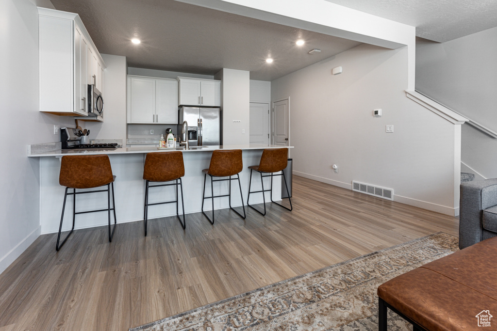Kitchen with appliances with stainless steel finishes, a peninsula, light wood-style flooring, white cabinetry, and recessed lighting