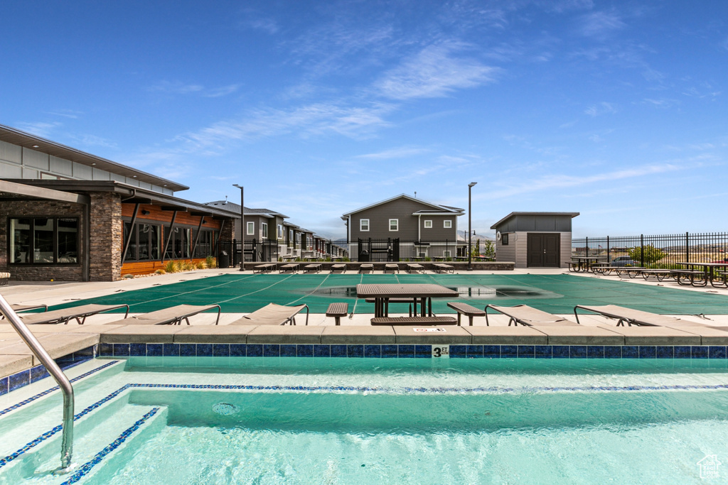 Community pool with fence, a storage shed, an outdoor structure, and a patio