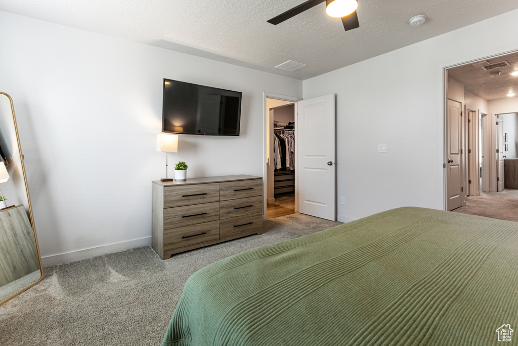 Bedroom featuring light colored carpet, a walk in closet, a ceiling fan, baseboards, and a closet