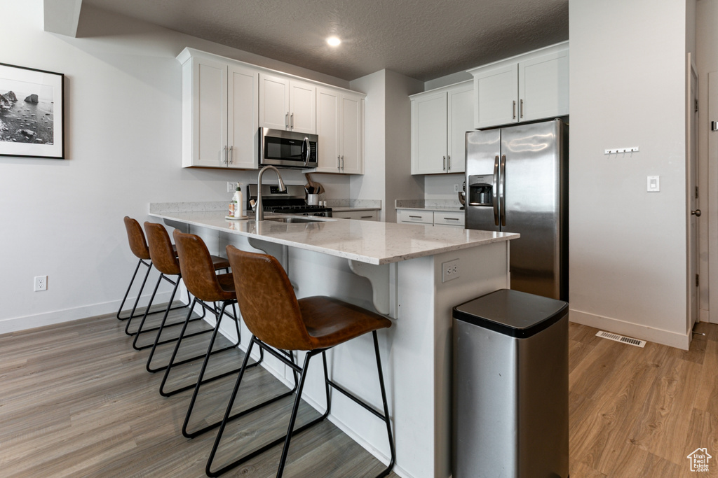 Kitchen featuring appliances with stainless steel finishes, baseboards, a peninsula, a kitchen bar, and light wood-style flooring