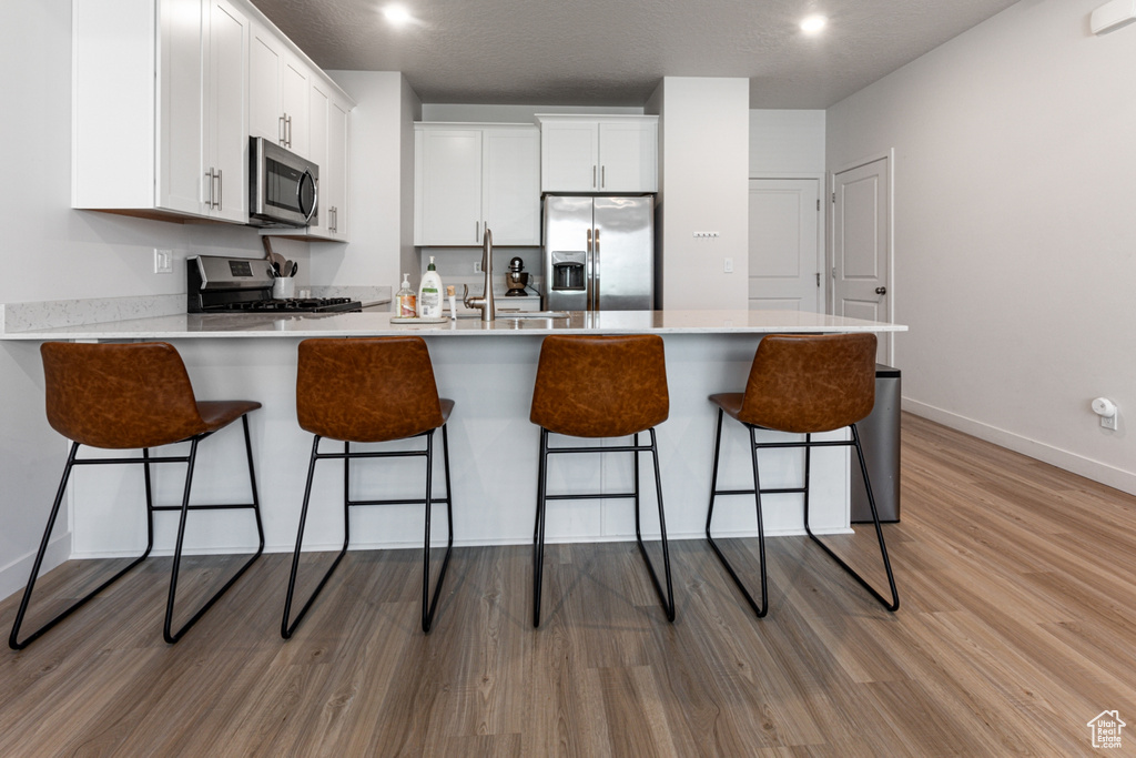 Kitchen featuring appliances with stainless steel finishes, a peninsula, light wood-style flooring, white cabinets, and a sink