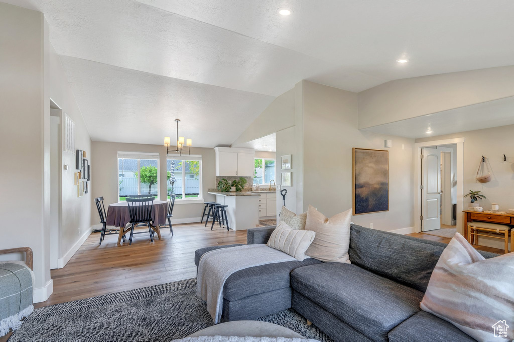 Living area featuring light wood-type flooring, a chandelier, lofted ceiling, recessed lighting, and baseboards