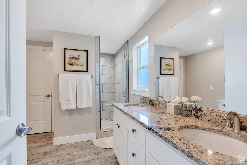 Bathroom featuring a shower stall, wood finish floors, baseboards, double vanity, and toilet