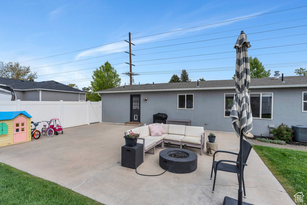 Rear view of house featuring a patio area, stucco siding, an outdoor living space with a fire pit, fence, and central AC unit