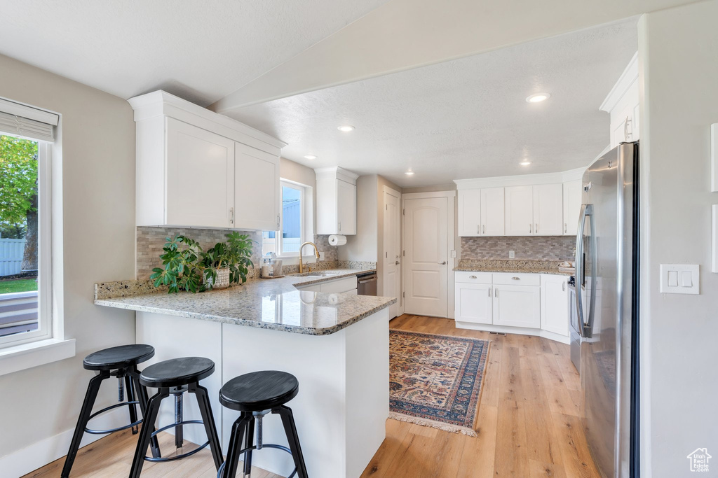 Kitchen with appliances with stainless steel finishes, a peninsula, decorative backsplash, a sink, and light stone counters