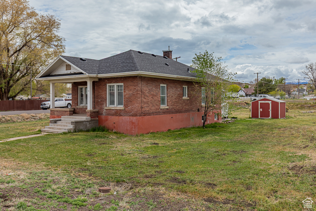 View of side of property with a shed, a shingled roof, brick siding, an outdoor structure, and a chimney