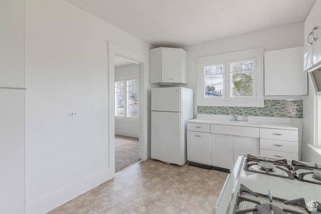 Kitchen featuring white appliances, white cabinetry, light countertops, a sink, and tasteful backsplash