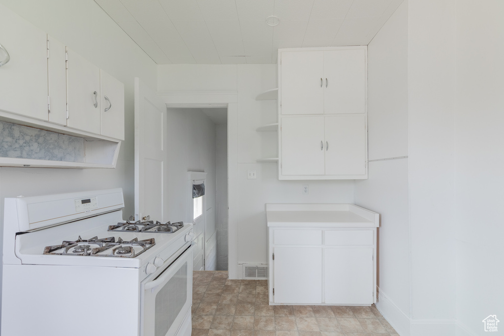 Kitchen featuring open shelves, white gas stove, light countertops, and white cabinets