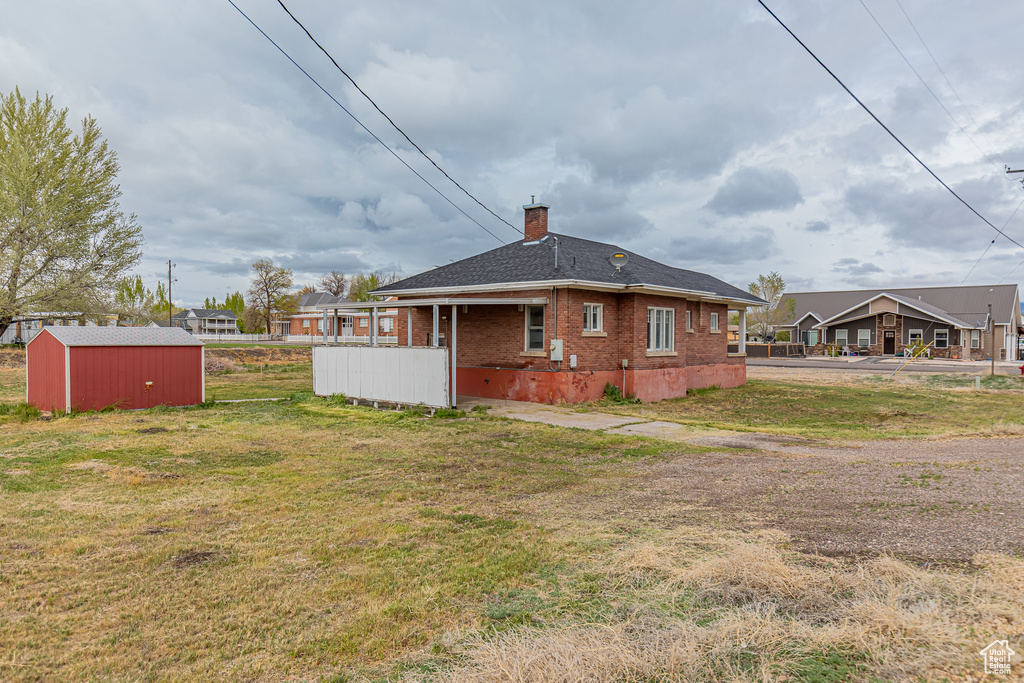 Rear view of house with a chimney, brick siding, a lawn, and an outdoor structure