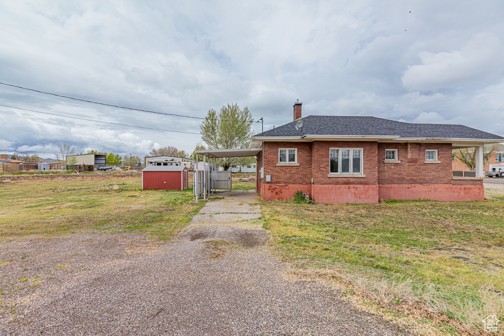 View of side of home featuring gravel driveway, brick siding, a chimney, a shed, and an outdoor structure