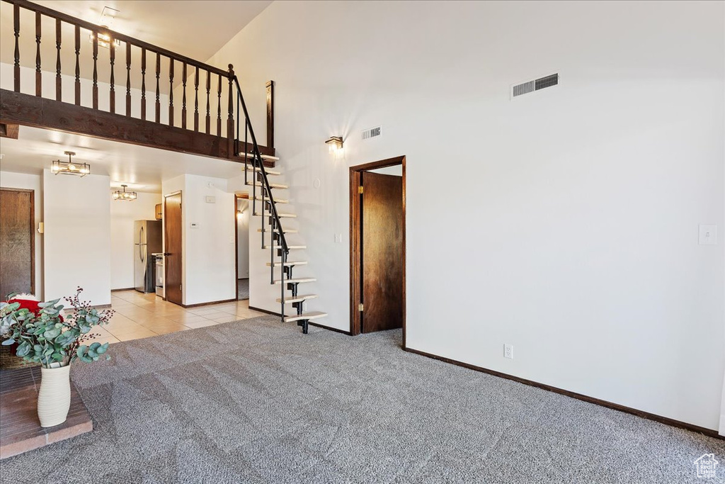 Unfurnished living room with a towering ceiling, light colored carpet, baseboards, stairway, and a chandelier