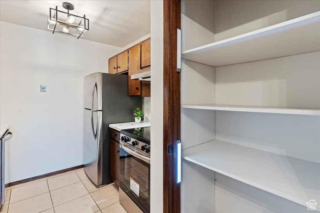 Kitchen with under cabinet range hood, stainless steel appliances, light countertops, baseboards, and light tile patterned floors