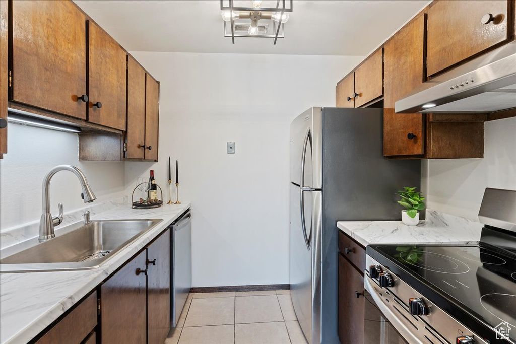 Kitchen featuring appliances with stainless steel finishes, under cabinet range hood, a sink, light tile patterned floors, and light countertops