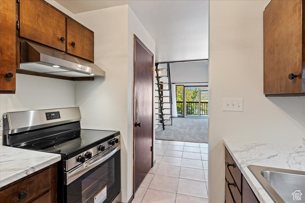 Kitchen with stainless steel range with electric cooktop, under cabinet range hood, light tile patterned flooring, and a sink