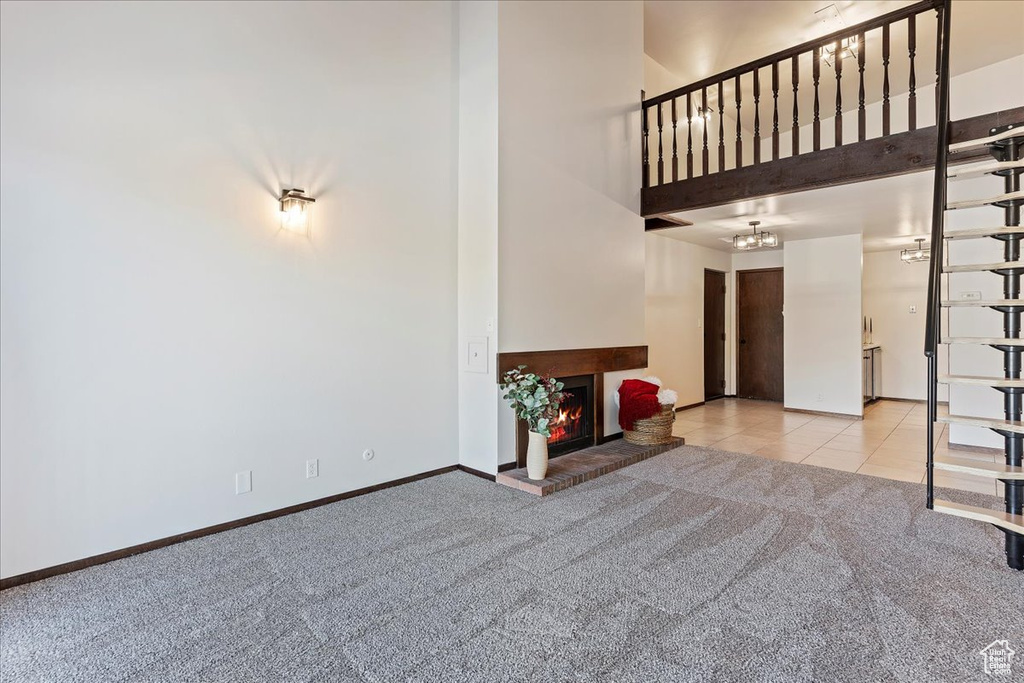 Unfurnished living room with a towering ceiling, carpet floors, a fireplace, a chandelier, and baseboards