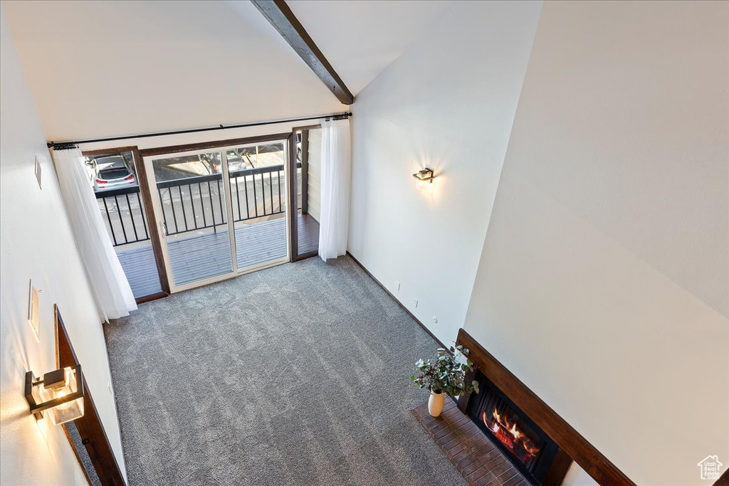 Unfurnished room featuring carpet, vaulted ceiling, and a lit fireplace