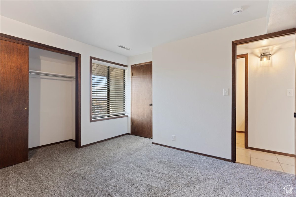 Unfurnished bedroom featuring light colored carpet, two closets, and baseboards