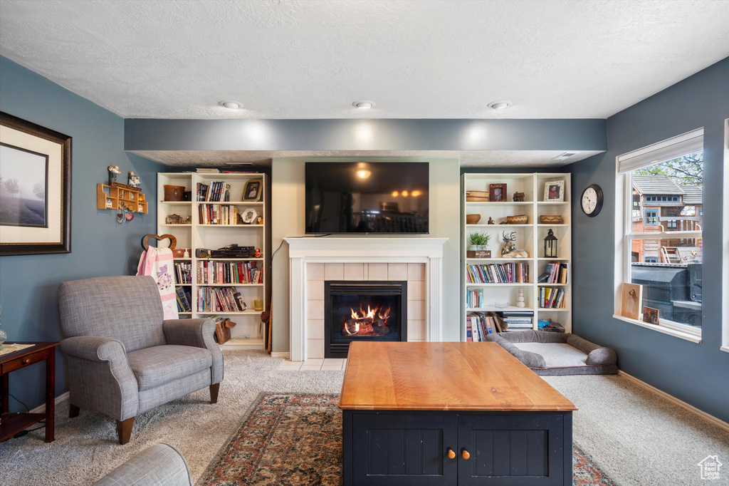 Living area with light colored carpet, a textured ceiling, a tiled fireplace, and baseboards