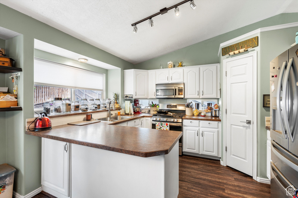 Kitchen featuring stainless steel appliances, a sink, dark countertops, white cabinetry, and lofted ceiling