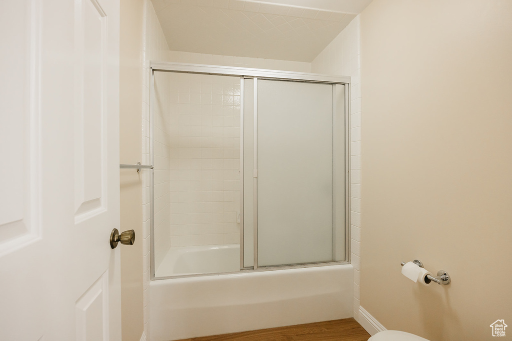 Full bath featuring combined bath / shower with glass door and wood finished floors