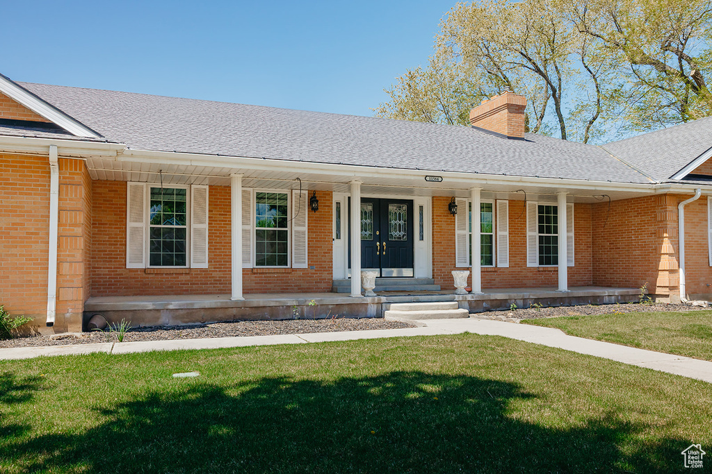 Single story home with covered porch, brick siding, a chimney, and a front lawn