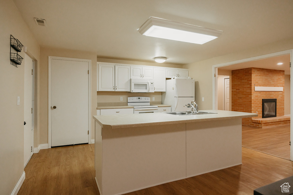 Kitchen with a sink, white appliances, visible vents, a fireplace, and white cabinetry